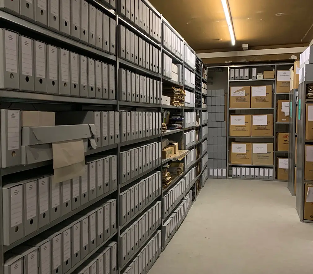 Das Bild zeigt Archivregale mit grauen Archivschachteln.