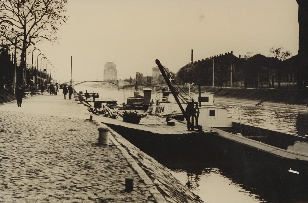 Das schwarz-weiß Foto zeigt das Ufer der Bega in Temeswar. Zu sehen ist ein Lastenschiff und Personen, die am Ufer spazierengehen.