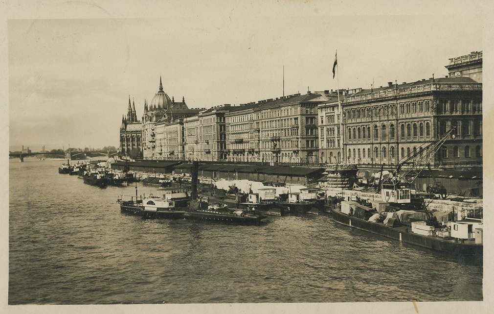 Das Foto zeigt eine Schwarz-Weiß-Ansichtskarte von Budapest. Zu sehen ist die Donau mit Schiffen sowie eine Häuserzeile direkt am Ufer.